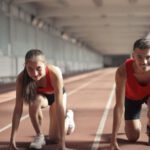 In-Demand Skills - Men and Woman in Red Tank Top is Ready to Run on Track Field