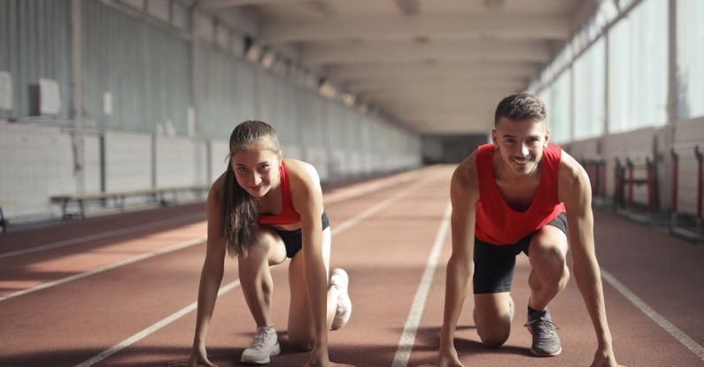 In-Demand Skills - Men and Woman in Red Tank Top is Ready to Run on Track Field
