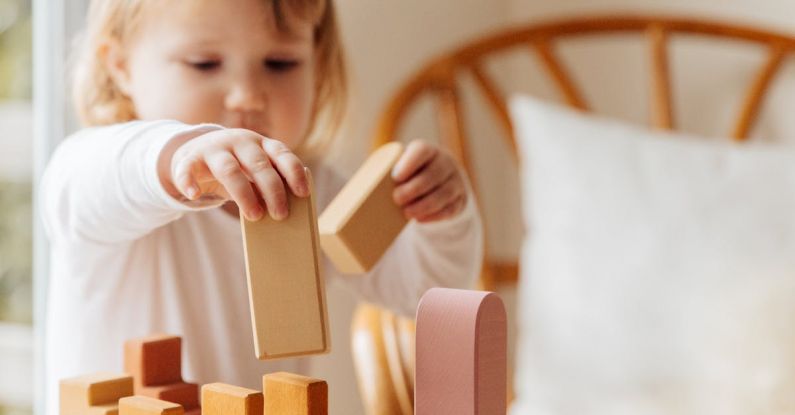 Educational Games - Cute little girl in white casual clothes standing near table and playing with wooden blocks while spending time at home