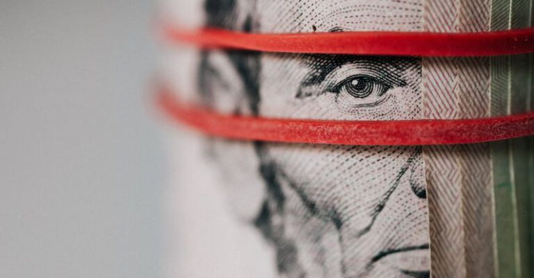 Money Mistakes - Closeup of rolled United States five dollar bills tightened with red rubber band