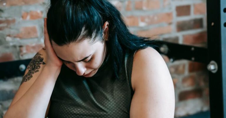 HIIT Workouts - Upset female sitting near sports equipment and feeling desperate and hopeless at training in fitness club