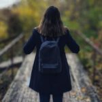 Solo Travel - Selective Focus Photography of Woman Wearing Black Overcoat Standing on Wooden Bridge