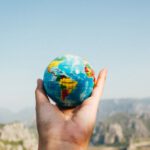 International Travelers - Person Holding World Globe Facing Mountain