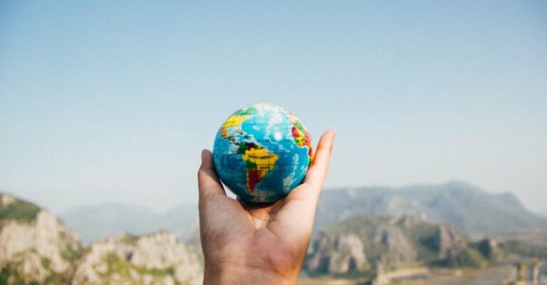 International Travelers - Person Holding World Globe Facing Mountain